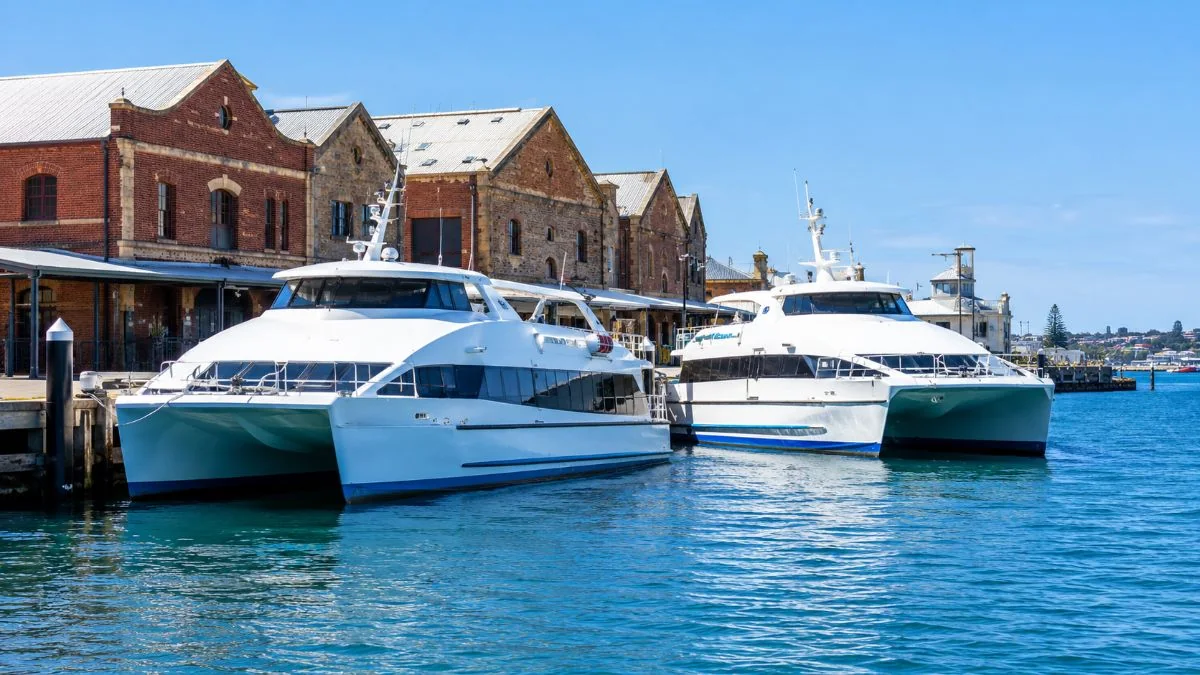 Two white passenger catamarans moored at a Fremantle wharf in front of old brick port sheds